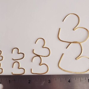 May include: Five gold-colored heart-shaped hoops of varying sizes. The hoops are arranged in a row from smallest to largest. The largest hoop is about 5 inches in diameter. The smallest hoop is about 1 inch in diameter.
