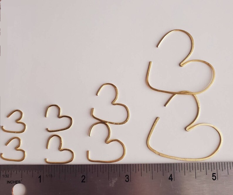 May include: Five gold-colored heart-shaped hoops of varying sizes. The hoops are arranged in a row from smallest to largest. The largest hoop is about 5 inches in diameter. The smallest hoop is about 1 inch in diameter.