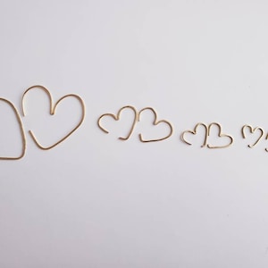 May include: Five gold heart-shaped hoops of varying sizes. The hoops are made of thin wire and are arranged in a row from largest to smallest.