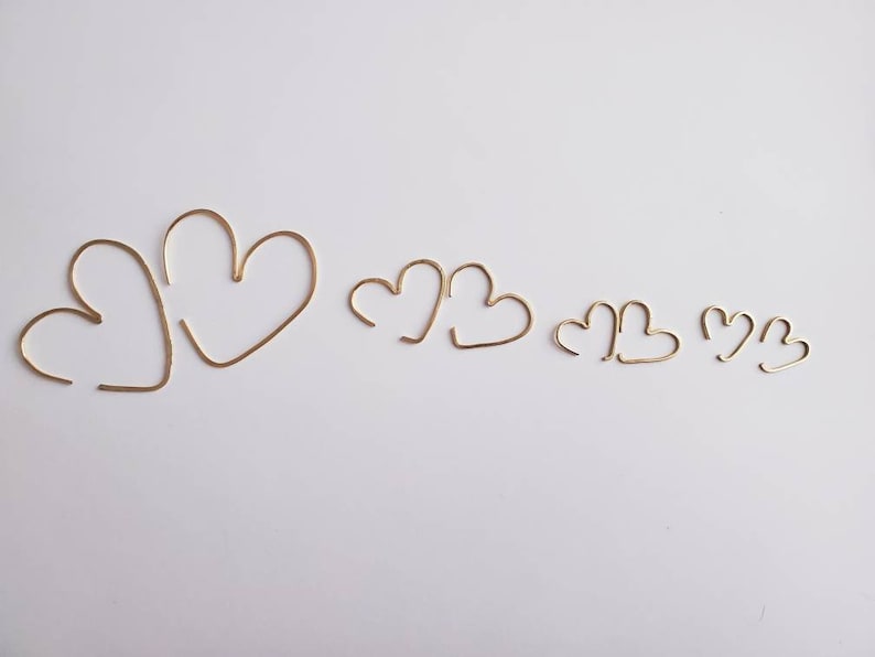 May include: Five gold heart-shaped hoops of varying sizes. The hoops are made of thin wire and are arranged in a row from largest to smallest.