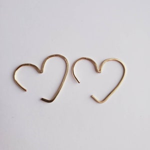 May include: A pair of gold heart-shaped hoop earrings. The earrings are made of thin wire and are simple and elegant.