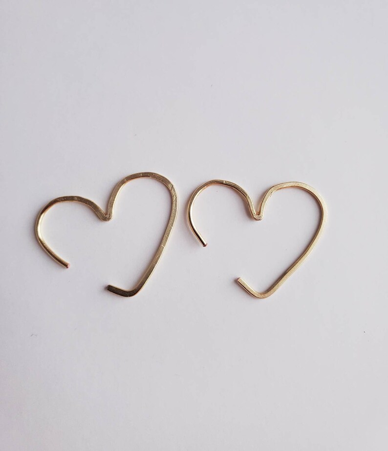May include: A pair of gold heart-shaped hoop earrings. The earrings are made of thin wire and are simple and elegant.