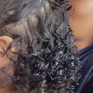 May include: A close-up of a young child with curly black hair, wearing a small hoop earring in their left ear. The child is being held by an adult with dark hair, who is wearing a gold hoop earring in their right ear.