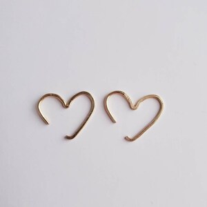 May include: A pair of gold heart-shaped hoop earrings. The earrings are simple and delicate, and would make a great gift for a loved one.