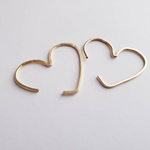 May include: Two gold heart-shaped hoop earrings. The earrings are simple and delicate, with a smooth finish.