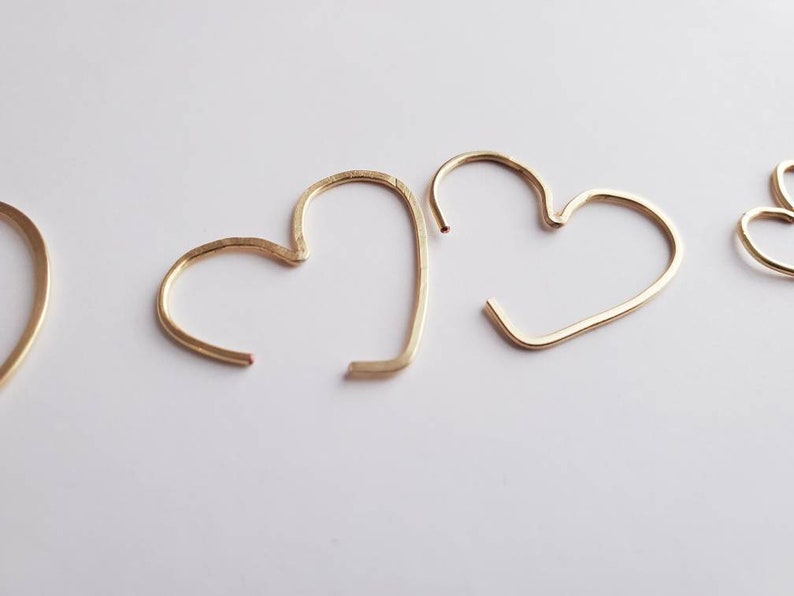 May include: Two gold heart-shaped hoop earrings. The earrings are simple and delicate, with a smooth finish.