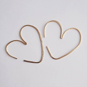 May include: A pair of gold heart-shaped hoop earrings. The earrings are made of thin wire and are simple and elegant.