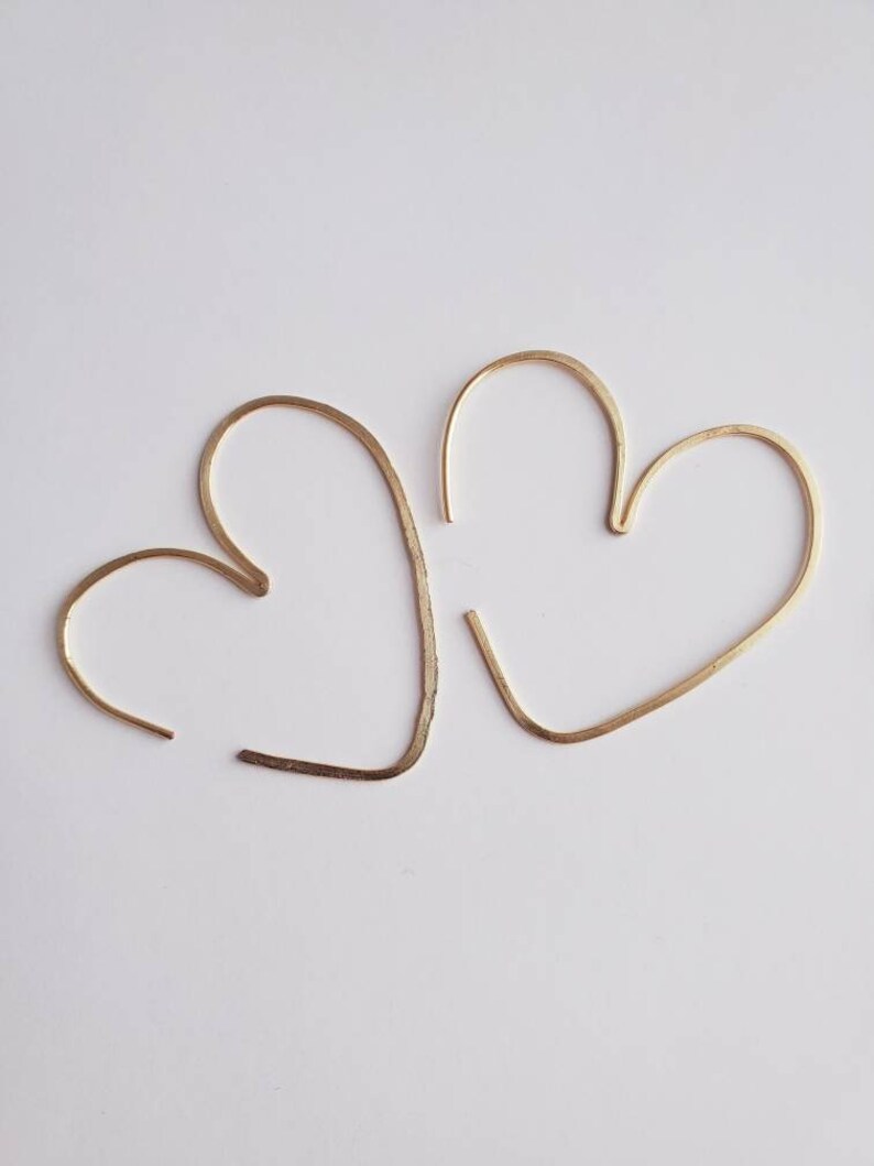 May include: A pair of gold heart-shaped hoop earrings. The earrings are made of thin wire and are simple and elegant.