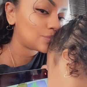 May include: A woman kisses a child on the forehead. The child is looking at a tablet screen with colorful handprints on it.