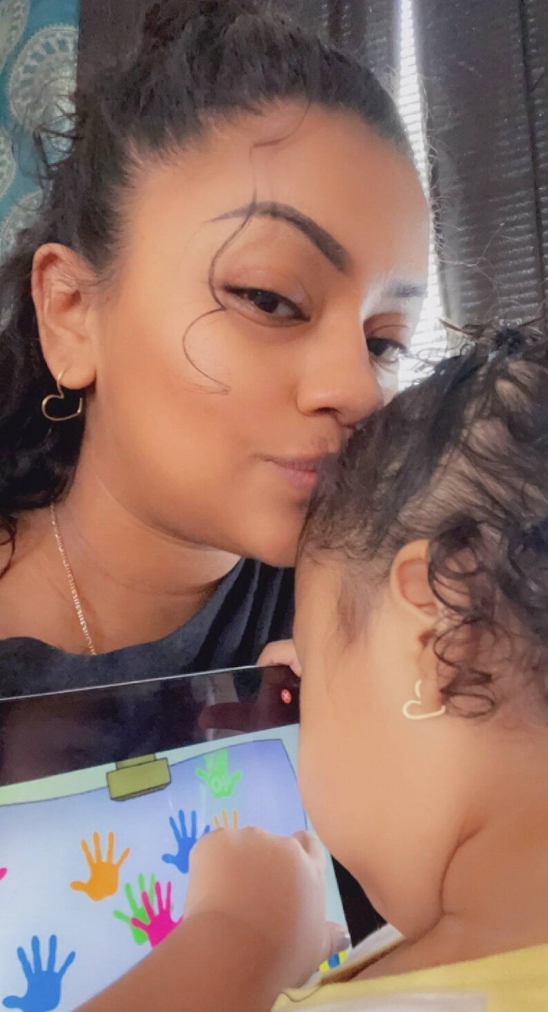 May include: A woman kisses a child on the forehead. The child is looking at a tablet screen with colorful handprints on it.