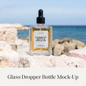 Puede incluir: Una botella cosmética de vidrio transparente con un tapón cuentagotas negro. La botella tiene forma rectangular y contiene un líquido dorado. La etiqueta dice "COSMETIC BOTTLE MOCK-UP". El fondo presenta rocas y el mar.