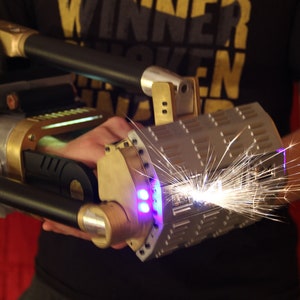 May include: A steampunk-style, hand-held device with a black handle, gold accents, and a silver, textured barrel. The device is emitting sparks from the end of the barrel.