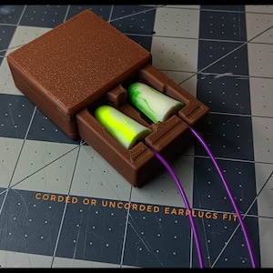 May include: A brown plastic case with two earplugs, one green and white and the other yellow and white. The earplugs are connected to the case with purple cords. The text "CORDED OR UNCORDED EARPLUGS FIT" is printed on the surface below the case.
