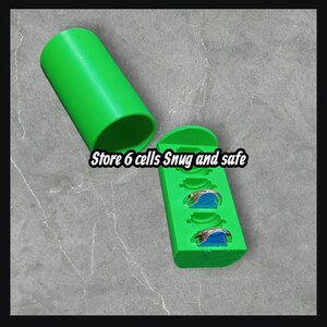 May include: A bright green storage container with a matching cylindrical lid. The container is open, revealing six compartments holding small, silver-colored objects with blue accents. Text on the container reads "Store 6 cells Snug and safe."