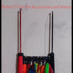 May include: A black wand holder with colorful feathers. The holder has a red handle and a black base. The feathers are in various colors, including red, orange, blue, yellow, and green. The text "Perfect Fit for the Accessories and Wands" is visible.
