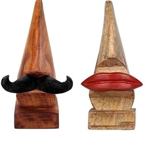 May include: Two wooden face-shaped holders with a mustache and red lips. The holders are made of wood and have a natural finish. They are perfect for holding jewelry, keys, or other small items.