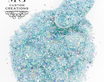 Könnte beinhalten: Ein Haufen hellblauer Glitter mit irisierendem Schimmer. Der Glitter befindet sich in einer kleinen Schaufel, wobei etwas auf eine weiße Oberfläche fällt.