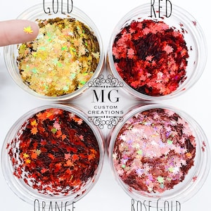 May include: Four clear plastic containers filled with leaf-shaped glitter in gold, red, orange, and rose gold colors. The word "GOLD" is above the gold glitter, "RED" above the red glitter, "ORANGE" above the orange glitter, and "ROSE GOLD" above the rose gold glitter. The logo "MG Custom Creations" is in the center.