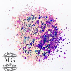 May include: A close-up of iridescent glitter in shades of pink, purple, and blue. The glitter is scattered on a white surface.