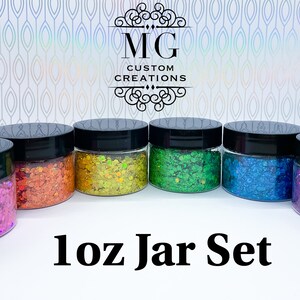 May include: Set of six 1 oz jars filled with colorful glitter. The jars have black lids and are arranged in a row. The text "1 oz Jar Set" is printed below the jars.