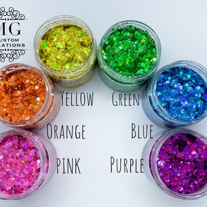 May include: Six small jars of glitter, each filled with a different color of glitter. The colors are orange, yellow, green, blue, pink, and purple. The jars are arranged in a circle, with the colors in a rainbow order.