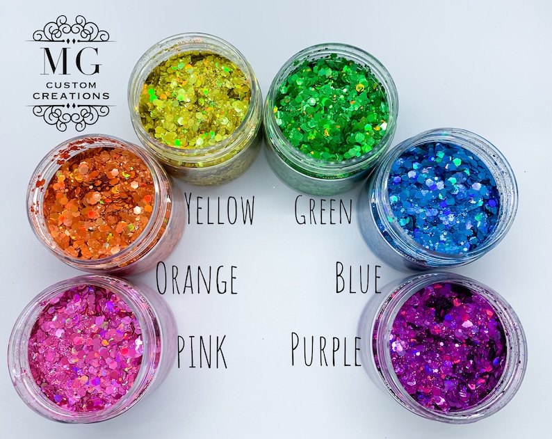 May include: Six small jars of glitter, each filled with a different color of glitter. The colors are orange, yellow, green, blue, pink, and purple. The jars are arranged in a circle, with the colors in a rainbow order.