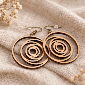 Könnte beinhalten: Ein Paar kreisförmige Holzohrringe mit einem ausgeschnittenen Spiraldesign. Die Ohrringe hängen an bronzefarbenen Metallhaken mit kleinen, durchsichtigen Kunststoffverschlüssen und zeigen eine natürliche braune Holzmaserung auf den kreisförmigen Formen.