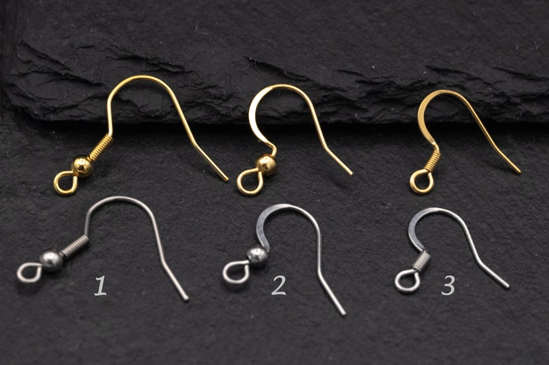 May include: An assortment of earring hooks in gold and silver tones. The hooks vary in design, including those with coiled springs, small beads, and simple curved shapes. The image is a close-up shot, showcasing the details of each hook.