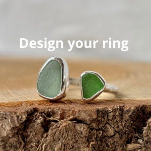 May include: Two rings with sea glass stones. One ring features a large, oval-shaped, pale green stone, while the other has a smaller, triangular, vibrant green stone. Both are set in silver. The text "Design your ring" is displayed above the rings.