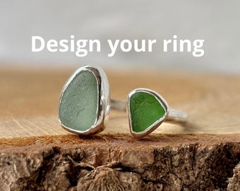 May include: Two rings with sea glass stones. One ring features a large, oval-shaped, pale green stone, while the other has a smaller, triangular, vibrant green stone. Both are set in silver. The text "Design your ring" is displayed above the rings.