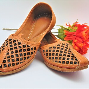 May include: A pair of brown leather shoes with a black lattice design. The shoes have a pointed toe and a flat sole.