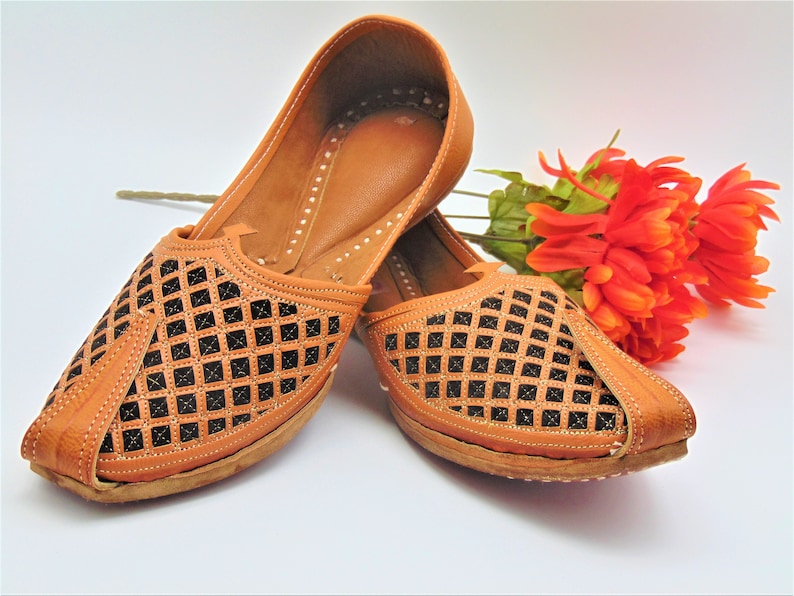 May include: A pair of brown leather shoes with a black lattice design. The shoes have a pointed toe and a flat sole.