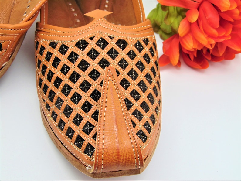 May include: Close-up of a pair of tan leather shoes with a black diamond pattern. The shoes have a pointed toe and are decorated with gold stitching.