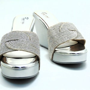 May include: A pair of silver wedge sandals with a rhinestone design. The sandals have a closed toe and a thick platform.