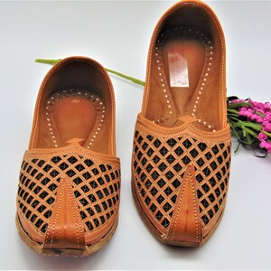 May include: A pair of brown leather shoes with a black diamond pattern cut-out design. The shoes have a pointed toe and a flat sole.