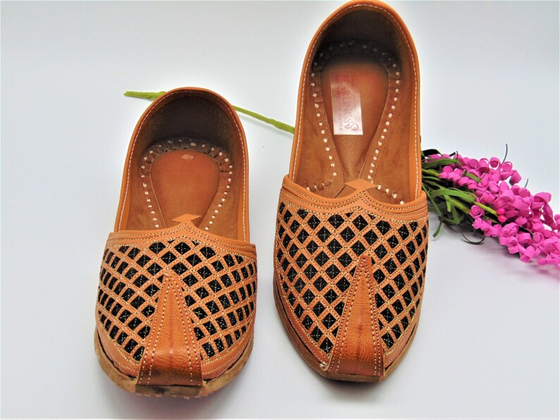 May include: A pair of brown leather shoes with a black diamond pattern cut-out design. The shoes have a pointed toe and a flat sole.