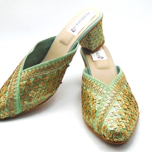 May include: A pair of mint green heeled mules with gold sequins and embroidery. The shoes have a pointed toe and a low heel.