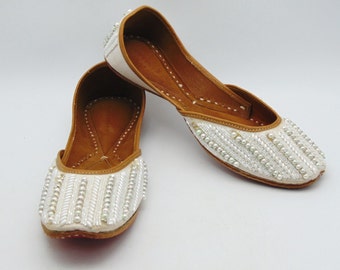 May include: A pair of white leather shoes with pearl embellishments. The shoes have a pointed toe and a low heel.