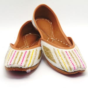 May include: A pair of white leather shoes with gold and pink beaded embellishments. The shoes have a pointed toe and a low heel.