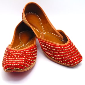 May include: A pair of red leather shoes with gold bead embellishments. The shoes have a pointed toe and a low heel.