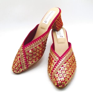 May include: A pair of pink sequined heeled mules with gold embroidery. The shoes have a pointed toe and a low block heel.