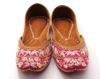 May include: A pair of pink embroidered flat shoes with gold and silver embellishments. The shoes have a brown leather insole and a pointed toe.
