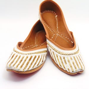 May include: A pair of white leather flats with gold and white beaded embellishments. The shoes have a pointed toe and a low heel.