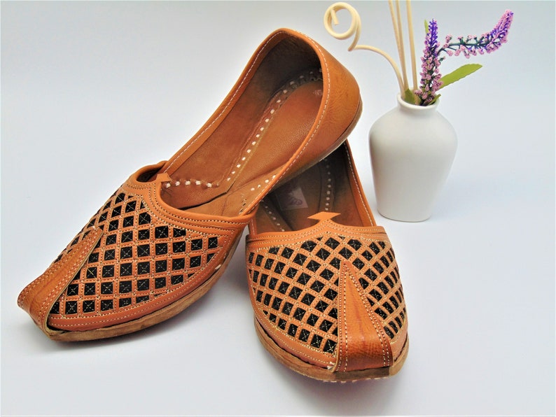 May include: A pair of brown leather shoes with a diamond-shaped cut-out pattern. The shoes have a pointed toe and a flat sole.