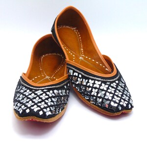 May include: A pair of black leather shoes with silver mirrored embellishments. The shoes have a pointed toe and a low heel. The shoes are made of a soft, supple leather and are perfect for any occasion.