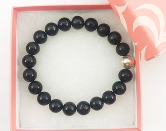 May include: A black beaded bracelet with a silver bead accent, displayed in a pink gift box.