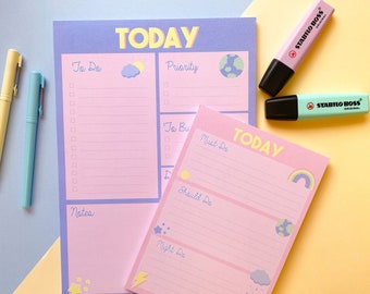 Op de afbeelding: Twee roze en paarse notitieblokken met het woord 'TODAY' bovenaan. Eén notitieblok heeft secties 'To Do', 'Priority' en 'Notes'. Het andere notitieblok heeft secties 'Must Do', 'Should Do' en 'Might Do'. Twee markeerstiften en twee pennen staan ook op de afbeelding.