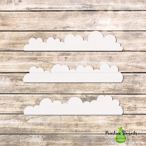 May include: Three white cloud-shaped stencils are displayed horizontally against a light brown wooden background. The stencils have a scalloped edge, resembling fluffy clouds. The bottom right corner features the Peartree Stencils logo.