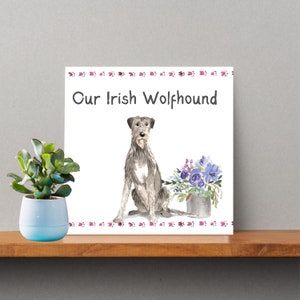May include: A white card with the text "Our Irish Wolfhound" and a watercolor illustration of a grey Irish Wolfhound sitting with a bouquet of purple flowers in a tin can.