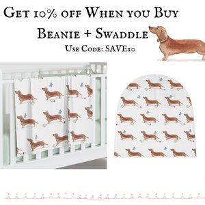 May include: A white swaddle blanket and beanie hat with a repeating pattern of brown dachshunds and blue butterflies. The text "Get 10% off when you buy beanie + swaddle. Use code: SAVE10" is at the top of the image.
